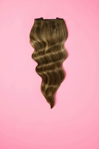 A collection of wavy hair extensions set against a pink backdrop, highlighting their luxurious appearance.