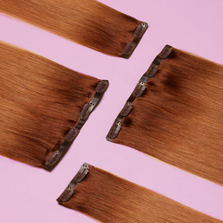 Four Brown clip-in Glam Seamless hair extensions on a light pink background.