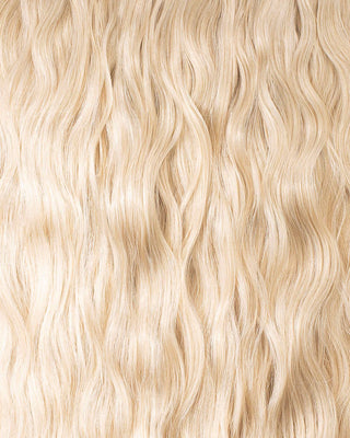 A close-up of long, wavy blonde hair extensions, showcasing their texture and shine.