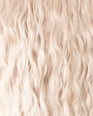 A close-up of long, wavy blonde hair extensions, showcasing their texture and shine in natural light.