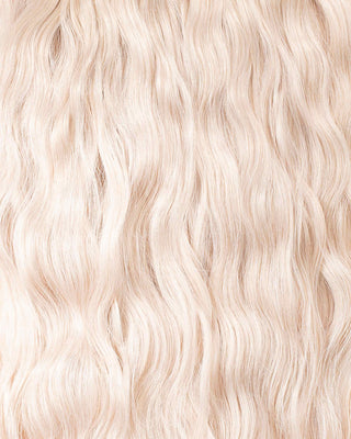 A close-up of wavy blonde hair extensions showcasing their texture and shine against a neutral background.