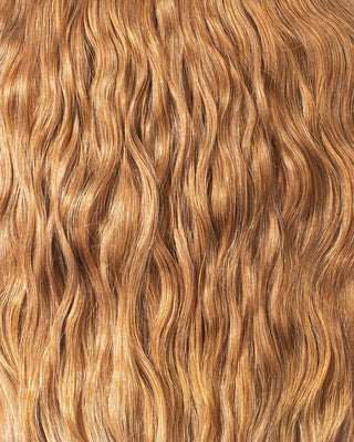 A close-up of long, wavy golden hair extensions, showcasing their luxurious texture and vibrant color.