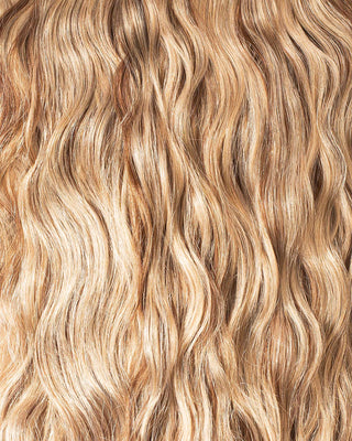 A close-up of wavy blonde hair extensions, showcasing their texture and shine in a vibrant, natural light.