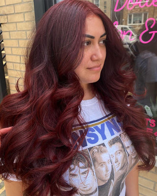 A woman with long wavy hair wearing a white top, and showing Glam Seamless Cherry Wine hair extension color