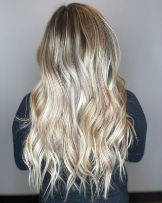 The back of the woman's head shows Glam Seamless cream beige balayage curled hair extensions.