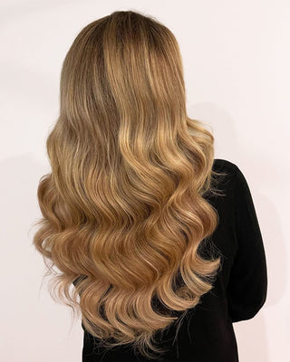 The back of a woman's head features long, wavy blonde hair, beautifully styled with hair extensions for added volume.