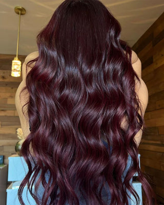 Woman with sleek, dark hair flowing down her back of Glam Seamless long wavy Mid Night Rose color hair extensions