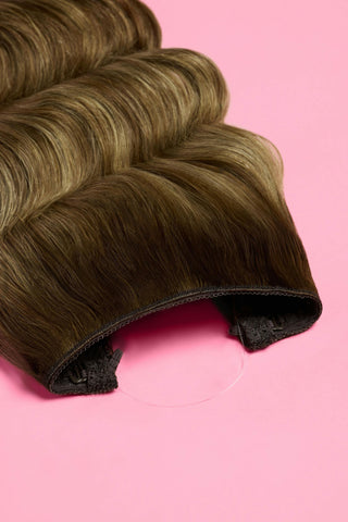 A wavy blonde hair extensions displayed against a soft pink background