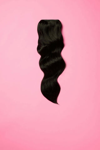 A single black wavy hair extension set against a vibrant pink background.